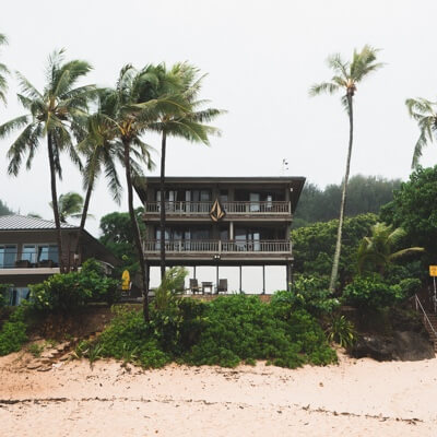 front of two storey house on sandy beach, with palm trees