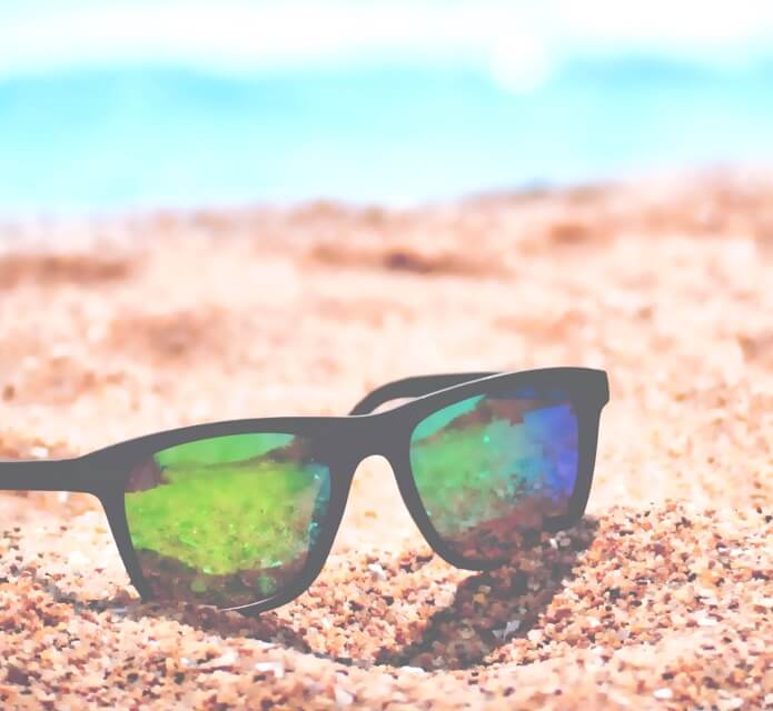 close up image of pair of sunglasses on sandy beach